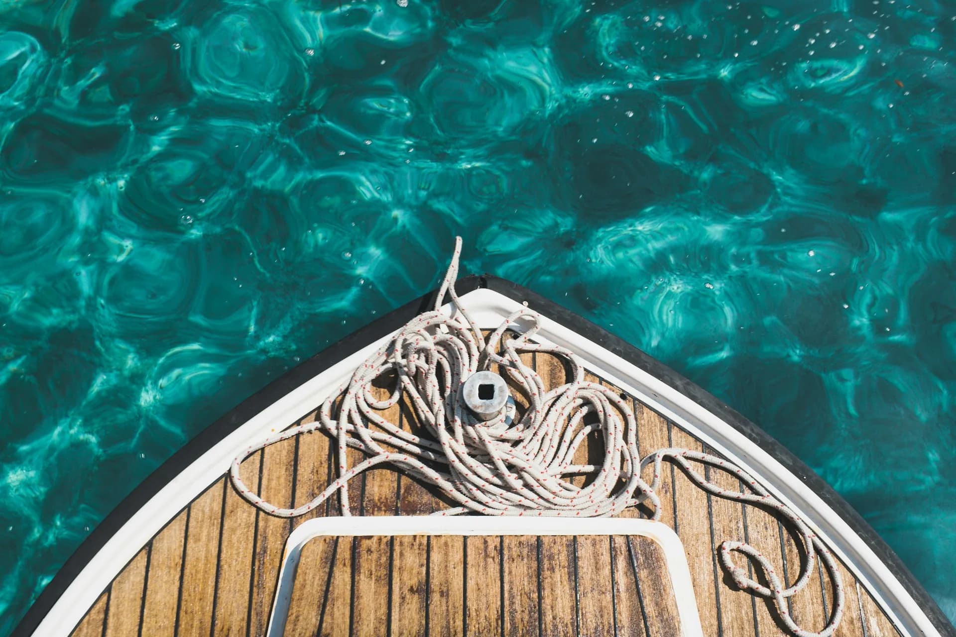 Proue en teck d'un bateau au mouillage sur une eau turquoise, cordage lové sur le pont